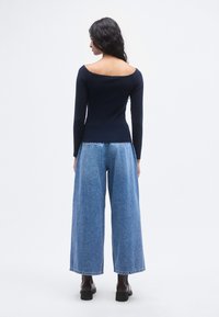 Μπλε ναυτικού χρώματος μακρυμάνικο τοπ με σχέδιο που αφήνει τους ώμους ακάλυπτους, σε συνδυασμό με ψηλόμεσα, φαρδιά τζιν παντελόνια μπλε χρώματος, με ακατέργαστο τελείωμα.