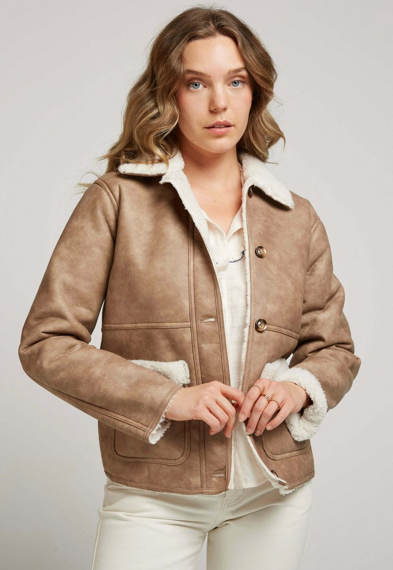 Veste en daim brun avec un col en fourrure, deux poches avant et fermeture à boutons. Design ajusté avec des finitions en fourrure blanche contrastante.