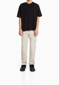 Black cotton t-shirt with short sleeves, paired with beige cargo pants featuring multiple pockets and a relaxed fit, worn with black sneakers.