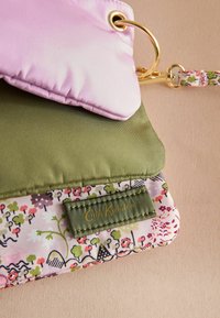 Mīkstināta aizskare rozā un olīvu zaļā krāsā ar ziedu raksta oderi, zelta aparatūru un teksturētu etiķeti ar uzrakstu "Cath Kidston".