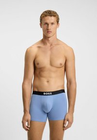 Hellblaue Boxershorts mit einem schwarzen elastischen Bund, der den Markennamen "BOSS" in Weiß zeigt. Das Material wirkt glatt und eng anliegend.