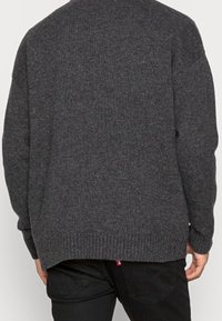 Maglione lavorato a maglia grigio scuro con polsini e orlo a coste. Vestibilità comoda, presenta un tessuto testurizzato e un collo alto.