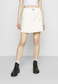 Biała i jasnozielona spódnica z elastycznym paskiem, bocznymi kieszeniami i warstwowymi falbanami, w zestawieniu z czarnymi botkami do kostki i białymi skarpetkami.