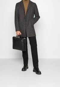Cappotto grigio a scacchi, due bottoni, tasche laterali. Maglione dolcevita marrone, pantaloni neri e borsa in pelle nera con manici. Stivali neri chunky.