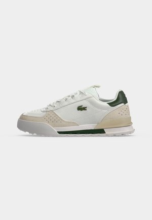 Λευκό και μπεζ χαμηλό sneaker με πράσινες λεπτομέρειες, διάτρητα πάνελ από σουέτ, λευκά κορδόνια και μικρό λογότυπο κροκόδειλου στο πλάι.