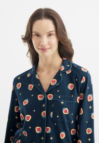 Granatowy zestaw piżamowy z wzorem w serca i gwiazdki, z kontrastującymi jasnoniebieskimi lamówkami i kieszenią na piersi. Wykonany z miękkiego materiału z zapięciem na guziki.