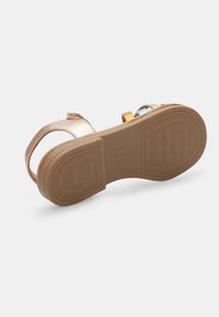 Beige, flache Sandale mit einer cuppierten Ferse. Sie verfügt über einen schmalen Riemen und metallische Akzente in Gold, Blau und Pink. Gummisohle mit strukturiertem Muster.