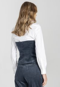 Biała koszula z długim rękawem w połączeniu z ciemnoniebieskim gorsetowym topem z sztruksu, charakteryzującym się pionowymi żeberkami i dopasowanym krojem.