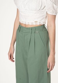 Lichtgroene wijde broek met plooien, elastische taille en accenten in zilver. Gecombineerd met een witte cropped blouse met kant.