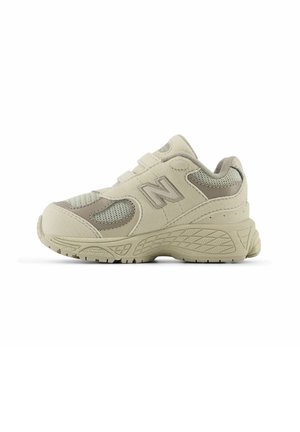 Beige athletic shoe with mesh side panels and padded collar. Features a textured rubber sole and Velcro strap for closure. New Balance logo visible.
