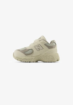 Beige athletic shoe with mesh side panels and padded collar. Features a textured rubber sole and Velcro strap for closure. New Balance logo visible.