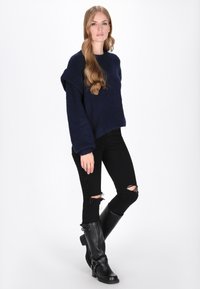 Marineblå, hyggelig strikket sweater med løs pasform og sænkede skuldre, parret med sorte slidte jeans og knælange sorte støvler med spænder.