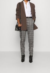 Brown blazer over a white shirt, gray plaid trousers, and black ankle boots. A black bag with a shoulder strap completes the outfit.