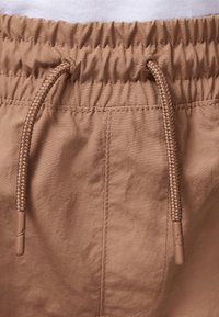 Close-up of brown elastic waistband with braided drawstring cords on lightweight fabric shorts or pants.