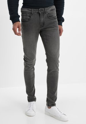 Jeans en denim gris avec une coupe slim, présentant des poches avant et une fermeture à bouton. Associés à des baskets blanches pour un look décontracté.