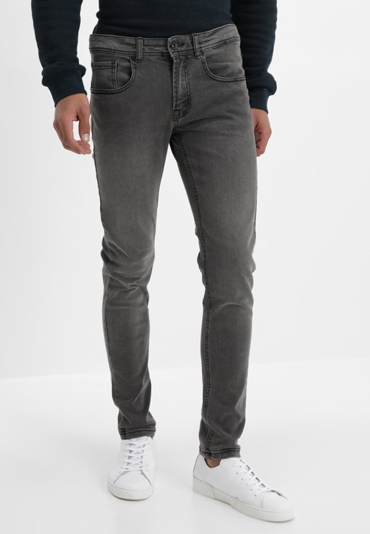 Jeans de mezclilla gris con un ajuste slim, que cuentan con bolsillos delanteros y cierre de botón. Combinándolos con zapatillas blancas para un look casual.