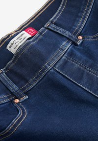 Legging sculptant en denim bleu foncé avec un design à enfiler. Comprend des éléments en cuivre, des coutures dorées contrastantes et une étiquette cousue à la taille.