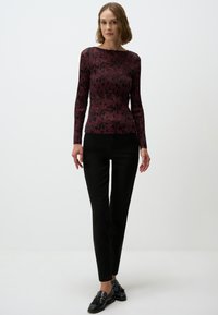 Lange mouw bordeaux top met een geribbelde textuur en zwart gespikkeld patroon, gecombineerd met zwarte slim-fit broeken en zwarte schoenen.