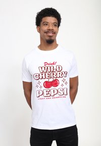 Bílý bavlněný tričko s červeným grafickým potiskem nápisu "WILD CHERRY PEPSI" spolu s třešněmi a třpytkami. Volný střih, kulatý výstřih.