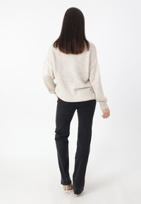Maglione beige lavorato a maglia con una vestibilità comoda, scollo rotondo e polsini a coste, abbinato a jeans neri slim-fit e tacchi beige.