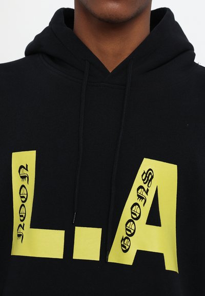 Hoodie noir avec de grands graphismes jaunes affichant "L.A" et des éléments textuels décoratifs ; tissu doux et détails avec capuche à cordon.