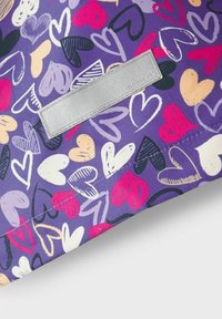 Lila Stoff mit einem sich wiederholenden Herzmuster in Pink, Weiß, Schwarz und Beige. Enthält ein kleines graues Etikett, das eingenäht ist.