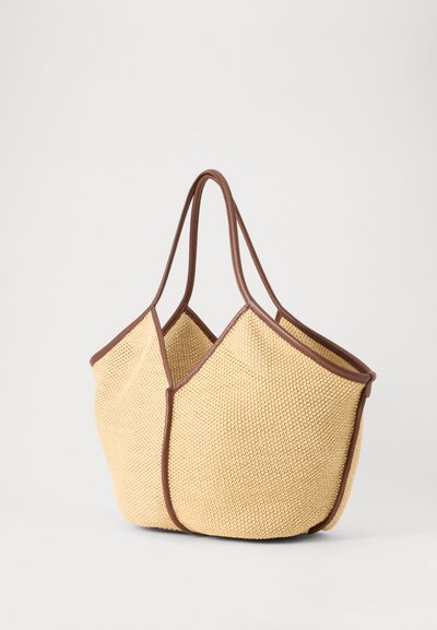 Sac fourre-tout tissé beige avec une bordure marron et deux anses, debout sur un fond clair uni.