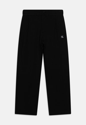 Pantaloni neri plissettati realizzati in un tessuto morbido. Presentano una vita con chiusura a bottone e un piccolo logo taglia sul lato. Vestibilità dritta e sartoriale.