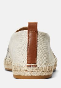 Espadrille de lona con un upper beige, acento de cuero marrón en el talón y suela de cuerda de yute. Superficie texturizada con detalles de costura visibles.