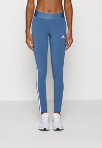 Blå atletiska leggings med en slät textur, med vita sidostråk och ett elastiskt midjeband. Enkla att kombinera med vita sneakers.