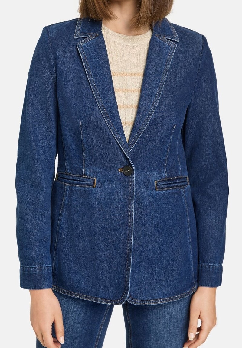 Femme portant un blazer en denim bleu foncé à un bouton sur un pull beige clair à rayures et un jean en denim assorti.