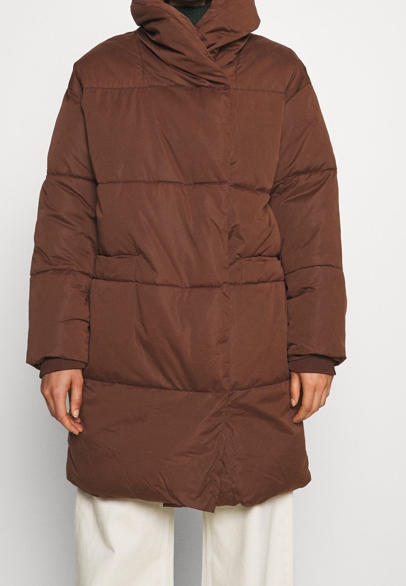 Hnědá péřová bunda s vysokým límcem, horizontálním prošíváním, předními kapsami a dlouhými rukávy, vyrobená z hladké, matné tkaniny.