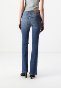 Uppvikta blå denimjeans med medeltvätt, med en etikett på baksidan och fyra fickor. Tyget har en slät yta.