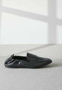 Mustad musta nahast loafers, millel on sile tekstuur, ümar nina, dekoratiivne rihm ja kortsus servad. Lame tall, minimaalistlik disain.