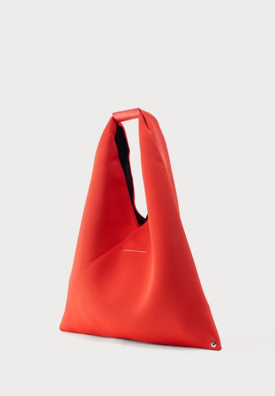 Κόκκινη υφασμάτινη τσάντα tote σε σχήμα τριγώνου με έναν ιμάντα και ένα μικρό μεταλλικό καρφί στο κάτω άκρο, εμφανίζεται σε απλό φόντο.