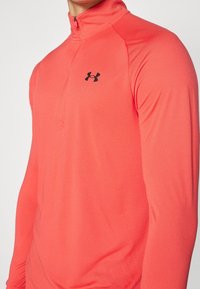 Pull à zipper corail fabriqué à partir d'un matériau lisse et extensible. Doté d'un col montant et d'un logo noir sur la poitrine gauche.