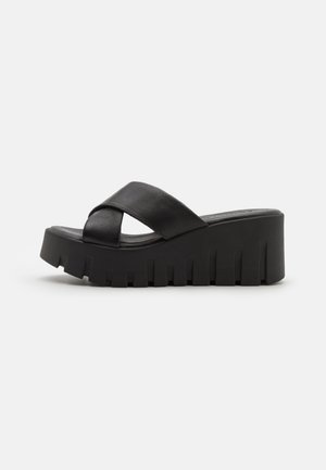 Black platform sandals with a cross-strap design. Made from smooth leather, featuring a thick, ridged sole for enhanced grip and stability.