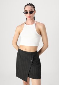 Gonna avvolgente a righe nere con due bottoni, abbinata a un crop top bianco a fascia. Gli occhiali da sole hanno una forma angolare a occhio di gatto.