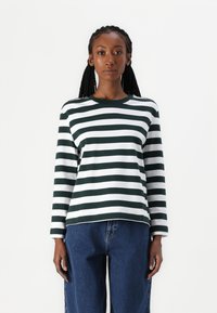 Maglietta a maniche lunghe a righe in verde scuro e bianco, con scollatura a girocollo e un taglio rilassato, abbinata a jeans blu larghi.