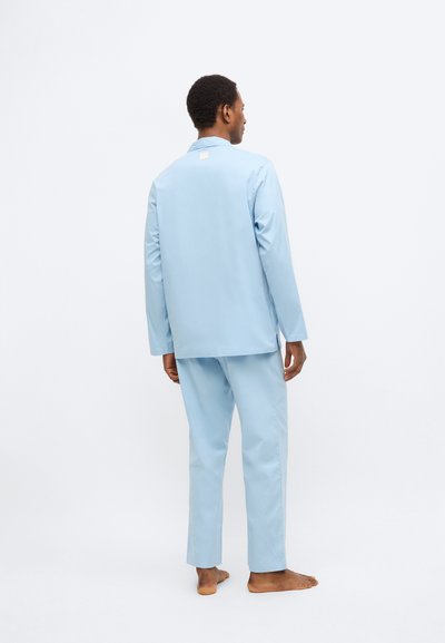 Svetlo modra sedežna garnitura iz gladkega blaga, ki vključuje dolg rokav in hlače s širokimi nogavicami, z oznako na zadnji strani.