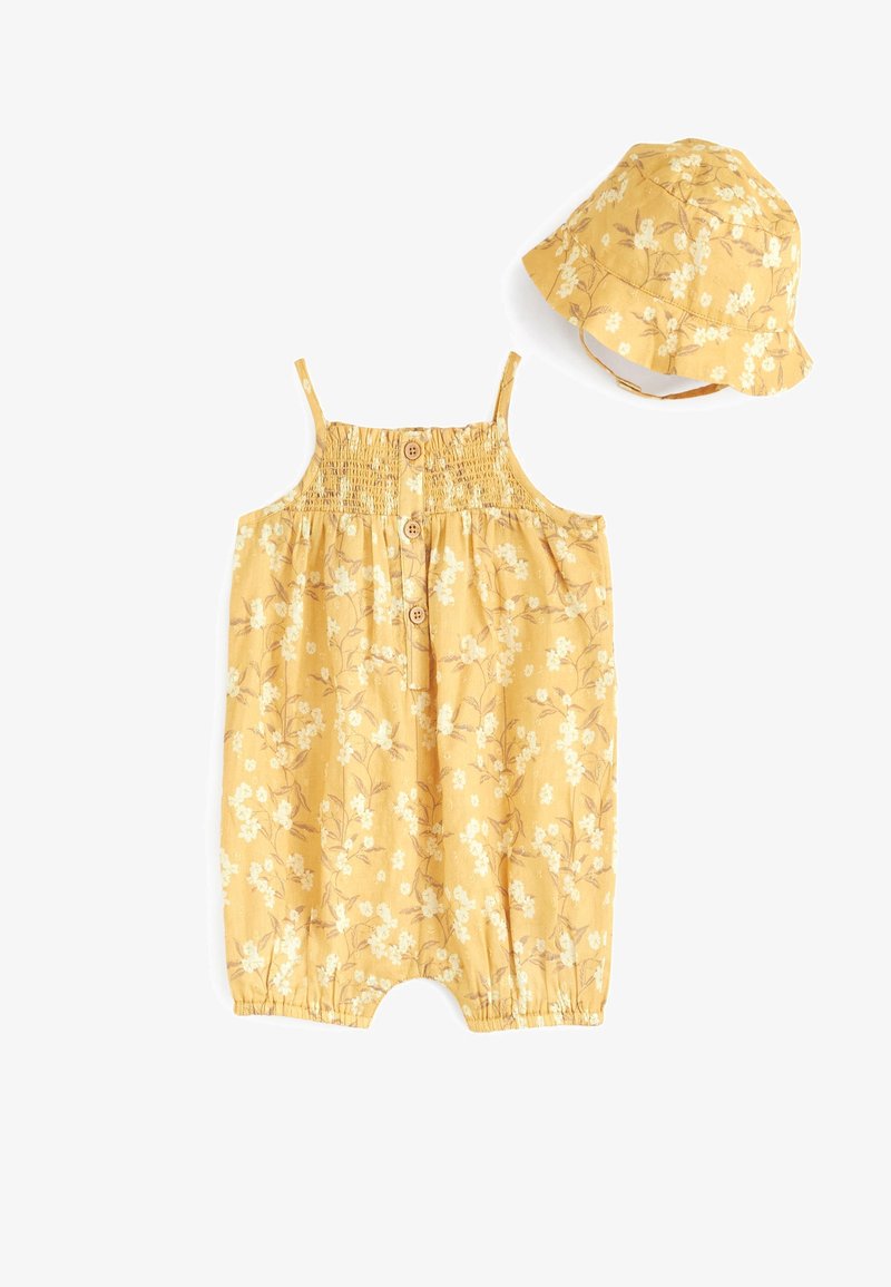 Barboteuse bébé jaune à fleurs sans manches avec boutons sur le devant et chapeau bob assorti avec bride sous le menton sur fond blanc.