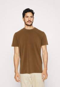 T-shirt marrone a maniche corte realizzato in morbido cotone, con colletto girocollo e un piccolo emblema sul petto, dal fitting confortevole.