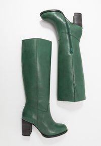 Bottes montantes vertes en cuir avec talon bloc, dotées d'une fermeture éclair latérale et de détails de coutures. Texture lisse avec une forme structurée.
