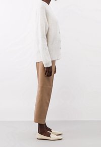 Hellbeige gestrickte Strickjacke mit V-Ausschnitt, drei Knöpfen und strukturierter Oberfläche; kombiniert mit hellbraunen Leder-Hosen im gerade Schnitt und cremefarbenen Ballerinas.