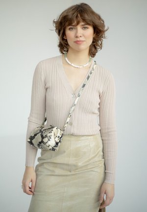 Cardigan a coste beige chiaro con bottoni, abbinato a una gonna dorata metallica. Accessoriato con una piccola borsa a tracolla in stampa serpente testurizzata.
