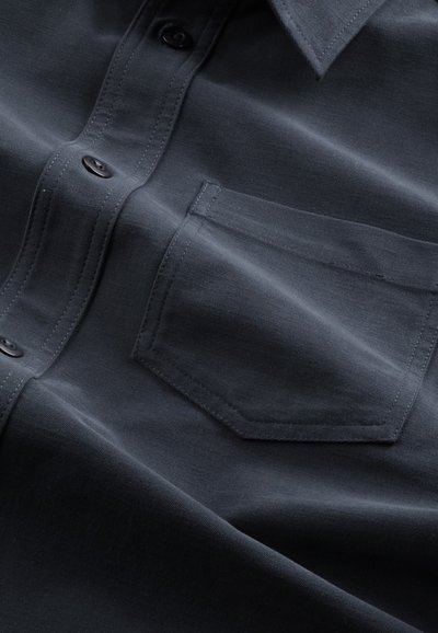 Dark blue button-up shirt with a chest pocket, featuring a smooth texture and subtle sheen, accentuated by black buttons and neat stitching.