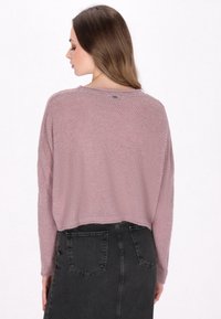 Kanten gebreide, korte trui in licht mauve met lange mouwen en een ronde halslijn, gecombineerd met een zwart denimrok met hoge taille.