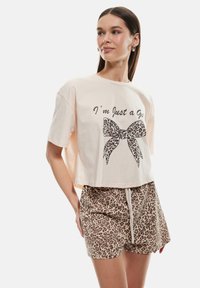 Camiseta de algodón corta de color rosa claro con el texto negro "Sólo soy una chica" y un lazo de estampado de leopardo. Combinada con pantalones cortos beige de estampado de leopardo.