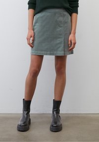 Jupe en coton vert à la coupe droite et à l'ourlet, associée à des bottines en cuir noir avec des semelles épaisses.