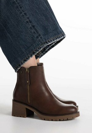 Stivaletti in pelle marrone con cerniera laterale e tacco a blocchetto, indossati con jeans a gamba larga blu scuro tagliati sopra la caviglia.